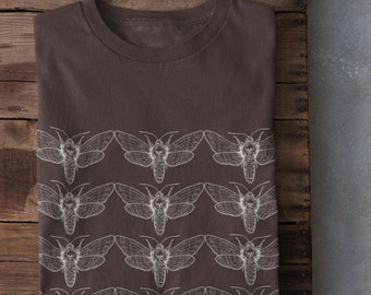 Puede incluir: Una camiseta marrón con un estampado blanco de un patrón repetido de polillas. Las polillas tienen un diseño de calavera en sus cuerpos.