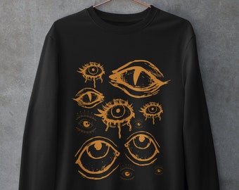 May include: Black sweatshirt with a graphic print of multiple stylized eyes in orange. The eyes are drawn in a variety of shapes and sizes, some with dripping tears.