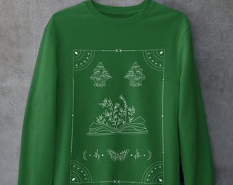 May include: A green sweatshirt with a white graphic design featuring a book, mushrooms, a butterfly, and geometric shapes.