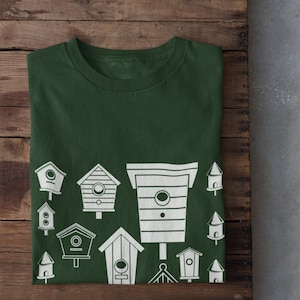 May include: A dark green t-shirt featuring a white design of various birdhouses. The design includes a variety of birdhouse shapes and sizes.