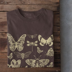 May include: A brown t-shirt with a vintage-style print of various butterflies and insects in a light yellow color.