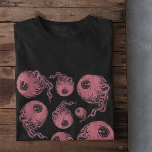 May include: Black t-shirt with a pink and white eye print design. The eyes are stylized and have a creepy, surreal look.