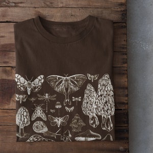 May include: A brown t-shirt with a white print of various insects and mushrooms. The print includes butterflies, moths, dragonflies, snails, and mushrooms.