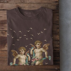 May include: A brown t-shirt with a print of two cherubs with wings, holding floral garlands and surrounded by flying birds.
