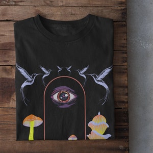以下が含まれることがあります： 大きな目、キノコ、鳥が描かれたサイケデリックなデザインの黒いTシャツ。目はピンクとオレンジのアーチで囲まれています。鳥は目の周りを円を描くように飛んでいます。