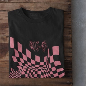 May include: Black t-shirt featuring a pink and black checkered pattern with three figures in the centre. The checkered pattern is distorted to create a wavy effect.