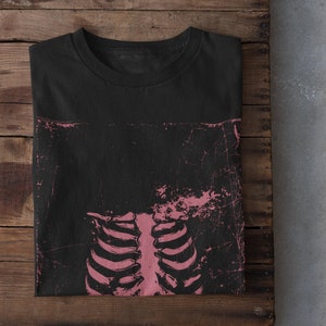 May include: Black t-shirt featuring a pink ribcage graphic print. The print has a distressed look and is centred on the shirt.