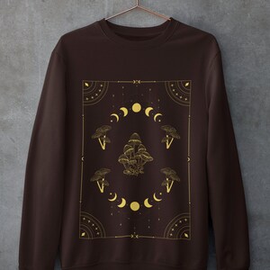 May include: A brown sweatshirt with a gold graphic design featuring mushrooms and moons in a geometric pattern.