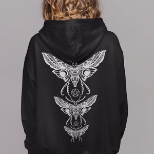 May include: Black hooded sweatshirt with a white graphic print of three moths on the back. The moths are arranged vertically, with the largest moth at the top and the smallest moth at the bottom. Each moth has a detailed design with intricate wings and a central body.