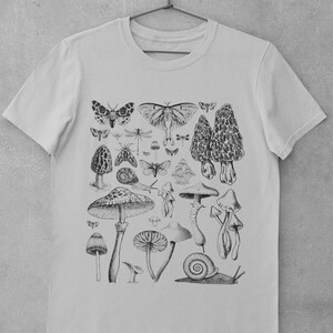 Puede incluir: Una camiseta gris claro con una ilustraci&oacute;n en blanco y negro de setas, mariposas y un caracol. La ilustraci&oacute;n est&aacute; centrada en la camiseta.