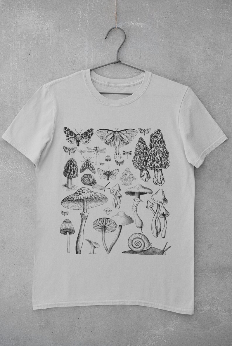 Puede incluir: Una camiseta gris claro con una ilustraci&oacute;n en blanco y negro de setas, mariposas y un caracol. La ilustraci&oacute;n est&aacute; centrada en la camiseta.