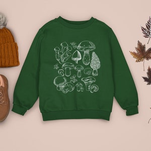 Puede incluir: Una sudadera verde con una ilustraci&oacute;n blanca de varios tipos de setas. La sudadera tiene cuello redondo y mangas largas.