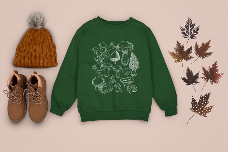 Puede incluir: Una sudadera verde con una ilustraci&oacute;n blanca de varios tipos de setas. La sudadera tiene cuello redondo y mangas largas.
