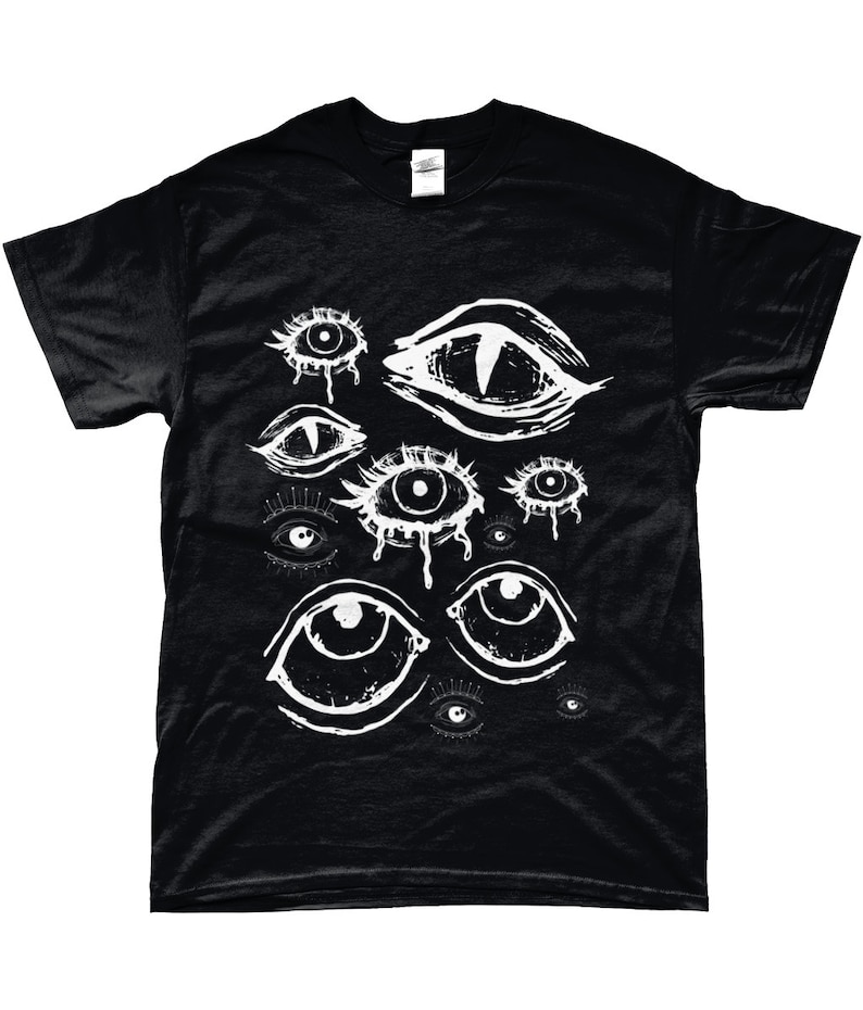 May include: Black t-shirt featuring a white graphic of various stylized eyes. The eyes have different shapes and sizes, some with teardrop details. The design is printed on a black, short-sleeved t-shirt.