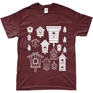 May include: A maroon t-shirt featuring a white design of various birdhouses in different shapes and sizes.