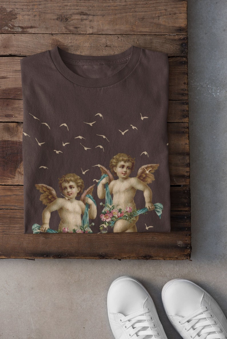 May include: A brown t-shirt with a print of two cherubs with wings, holding floral garlands and surrounded by flying birds.