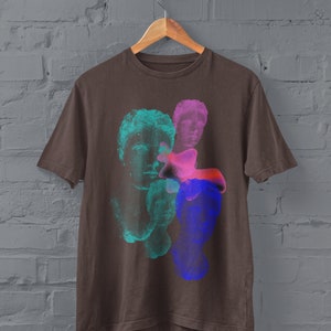 May include: A brown t-shirt with a graphic print of three colorful, abstract faces. The faces are in shades of blue, green, and pink.