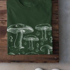Puede incluir: Una camiseta verde oscuro con un estampado blanco de varios hongos y hojas.