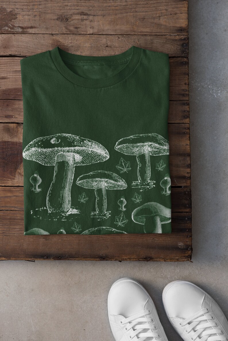 Puede incluir: Una camiseta verde oscuro con un estampado blanco de varios hongos y hojas.