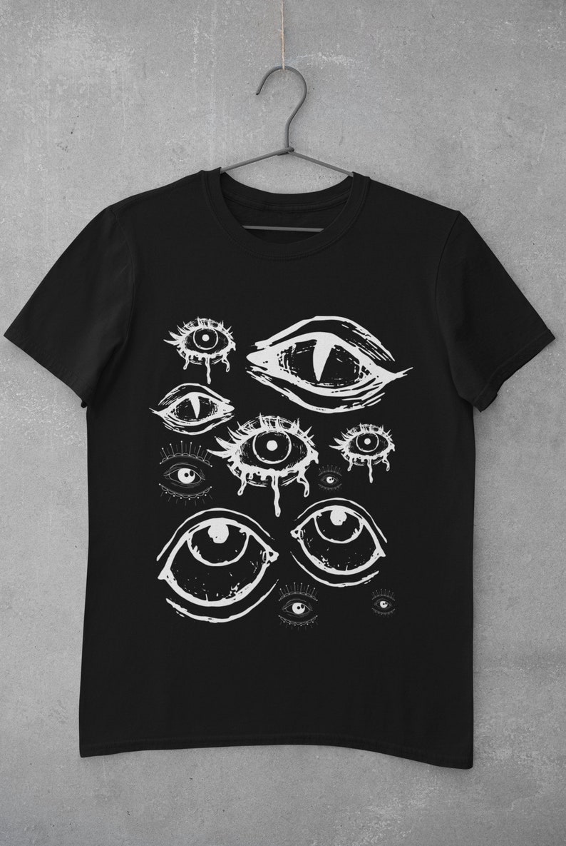 May include: Black t-shirt featuring a white graphic of various stylized eyes. The eyes have different shapes and sizes, with some appearing to be crying. The design is a bold, artistic statement, perfect for those who appreciate unique apparel.