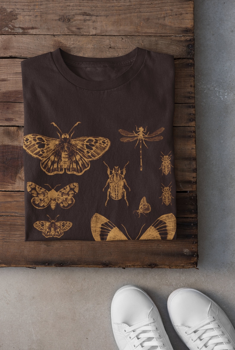 May include: A brown t-shirt with a gold print of various insects, including butterflies, beetles, and dragonflies.