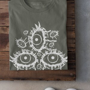 May include: A green t-shirt with a white graphic print of multiple eyes. The eyes are drawn in a stylized, dripping style.