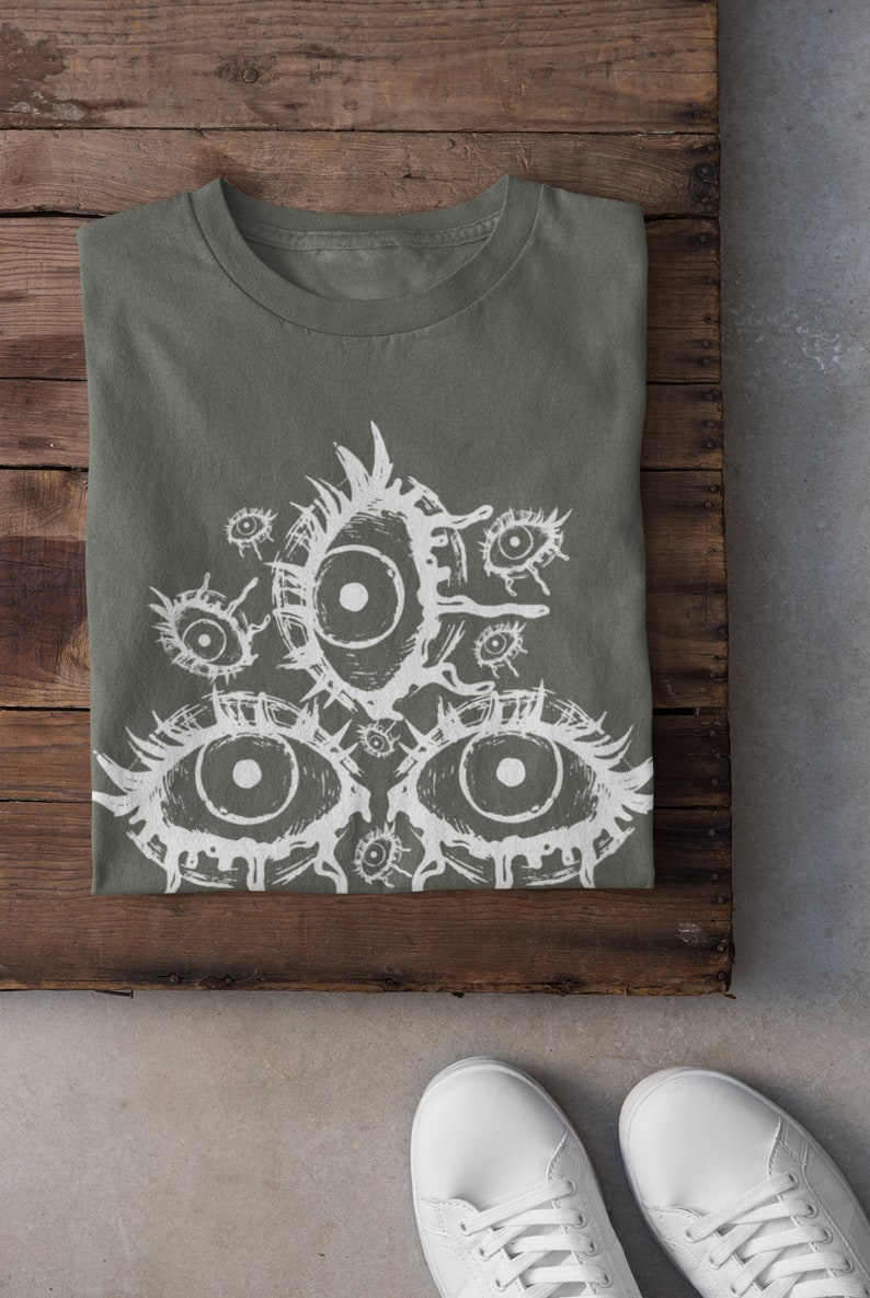 May include: A green t-shirt with a white graphic print of multiple eyes. The eyes are drawn in a stylized, dripping style.