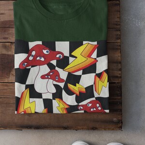 May include: A green t-shirt with a checkered pattern on the bottom half. The pattern features red mushrooms with eyes, yellow lightning bolts, and black and white squares.