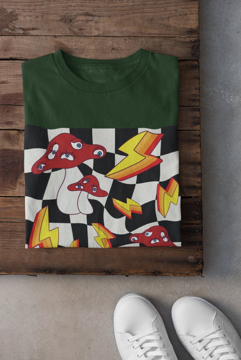 May include: A green t-shirt with a checkered pattern on the bottom half. The pattern features red mushrooms with eyes, yellow lightning bolts, and black and white squares.