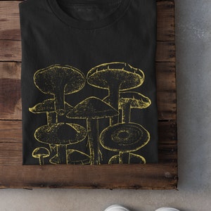 Pode incluir: Camiseta preta com um gr&aacute;fico amarelo de um grupo de cogumelos.