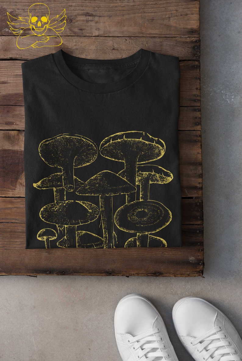Pode incluir: Camiseta preta com um gr&aacute;fico amarelo de um grupo de cogumelos.