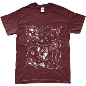 May include: A maroon t-shirt with a white design of various animal skulls, insects, and a rabbit. The design includes a monkey skull, a ram skull, a rat skull, a bird skull, and a rabbit head.