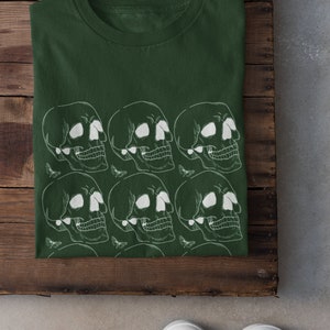 May include: A dark green t-shirt with a white skull and moth pattern. The shirt is folded and laid on a wooden surface.