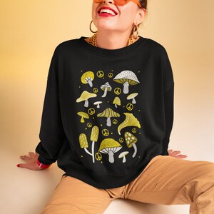 Puede incluir: Sudadera negra con un estampado gr&aacute;fico de setas amarillas y blancas. El estampado presenta varios tipos de setas con s&iacute;mbolos de paz.