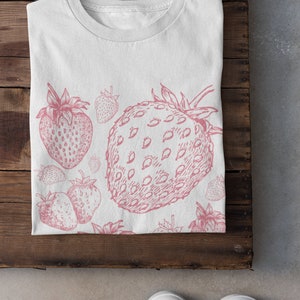May include: White t-shirt with a pink strawberry print. The strawberries are drawn in a vintage style with detailed seeds and leaves.