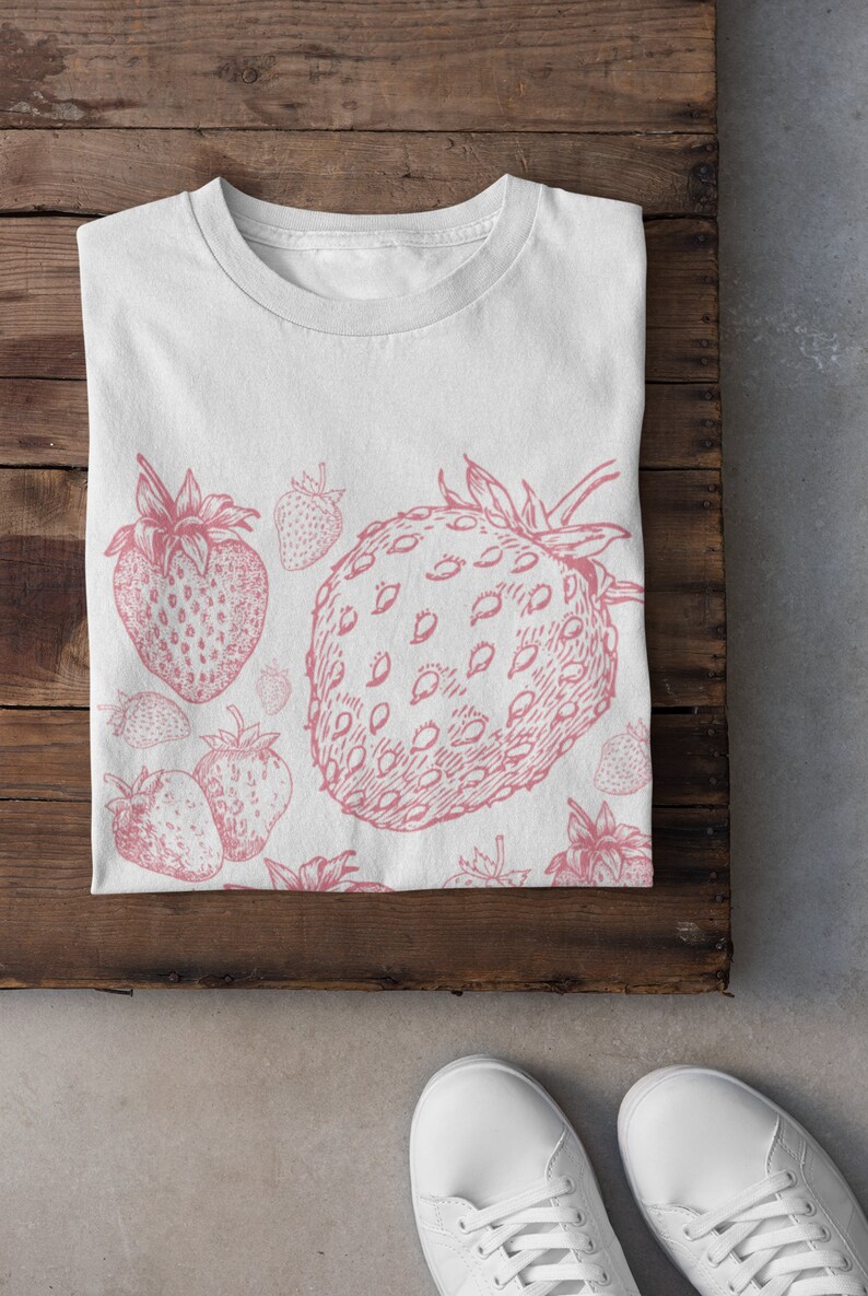 May include: White t-shirt with a pink strawberry print. The strawberries are drawn in a vintage style with detailed seeds and leaves.