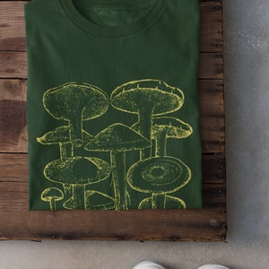 Pode incluir: Uma camiseta verde escura com uma estampa gr&aacute;fica amarela de um grupo de cogumelos.