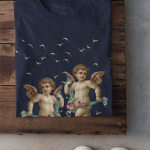May include: A navy blue t-shirt with a print of two cherubs with wings and floral garlands, flying against a background of white birds.