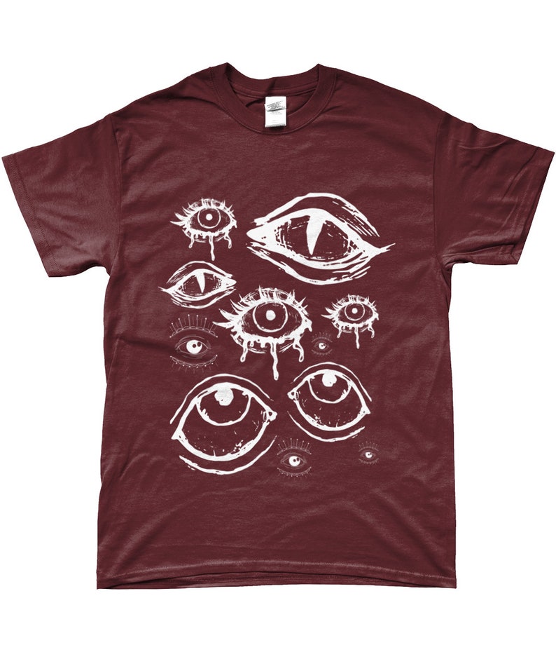 May include: Burgundy t-shirt featuring a white graphic of multiple stylized eyes. The eyes vary in size and style, some with teardrop details. The shirt is made of a soft material and has a classic crew neck.