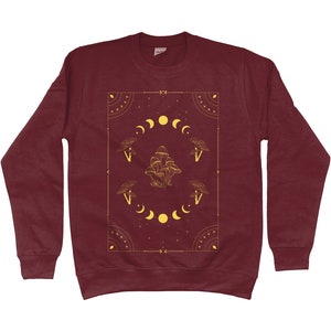 May include: Burgundy sweatshirt with a gold graphic design featuring mushrooms and moons in a geometric frame.