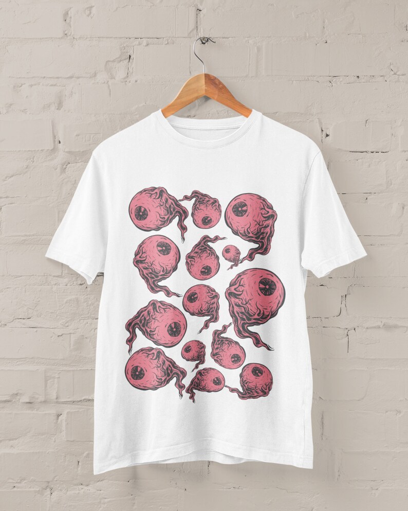 May include: White t-shirt with a graphic print of pink eyes with black outlines and smoke-like trails. The eyes are arranged in a random pattern on the shirt.