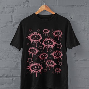 May include: Black t-shirt with a pink graphic print of multiple dripping eyes and stars.