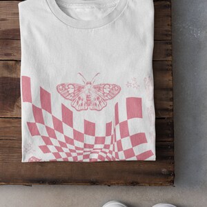 May include: White t-shirt with a pink checkered pattern and a butterfly graphic. The pattern is distorted to create a 3D effect.