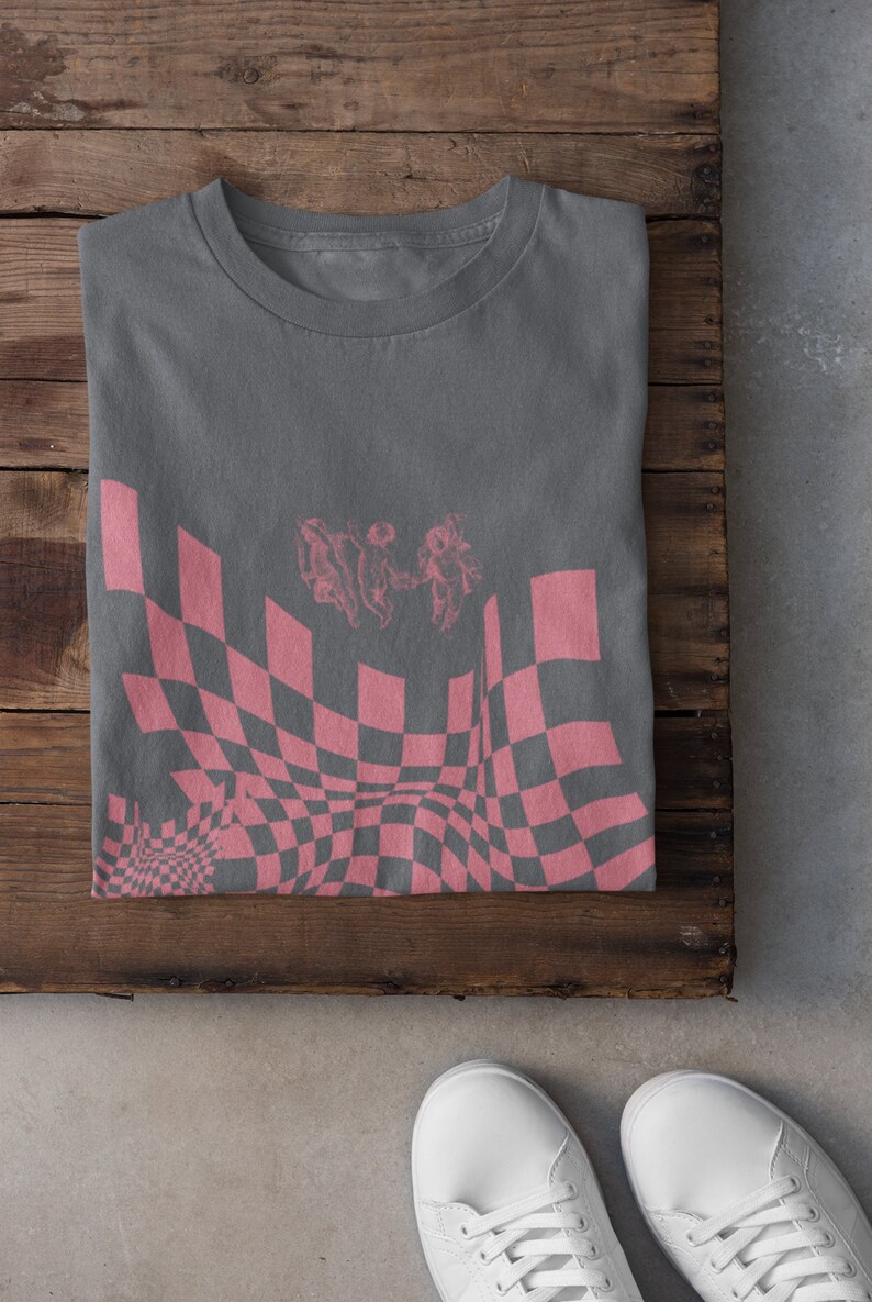 May include: A grey t-shirt with a pink checkered pattern and a graphic of three figures in a distorted perspective.