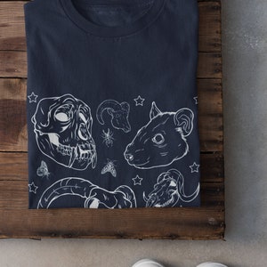 May include: A navy blue t-shirt with a white graphic print of various animal skulls, including a ram, a rat, and a monkey. The graphic also includes stars and insects.