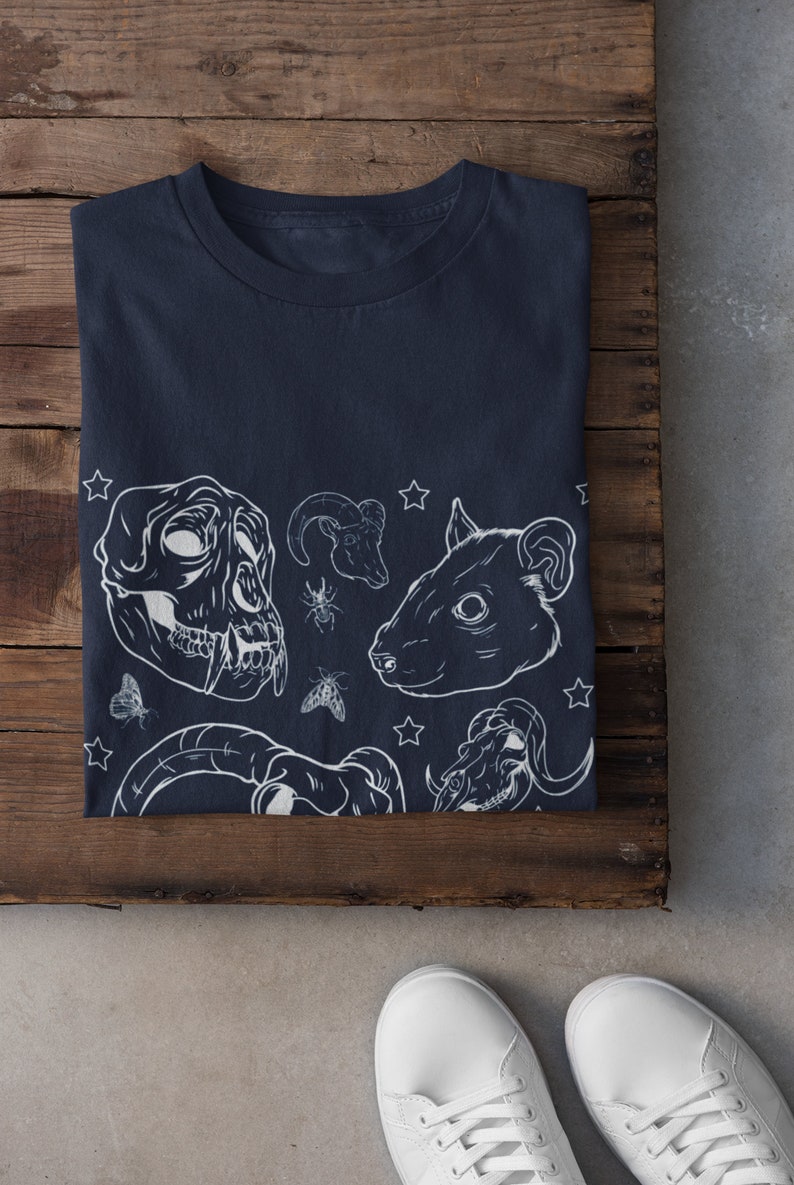 May include: A navy blue t-shirt with a white graphic print of various animal skulls, including a ram, a rat, and a monkey. The graphic also includes stars and insects.