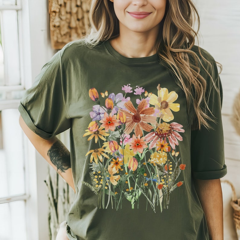 May include: A green t-shirt with a colorful floral print. The flowers are painted in a watercolor style and include shades of pink, orange, yellow, and purple.