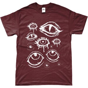 May include: A maroon t-shirt with a white graphic print of multiple stylized eyes. The eyes are drawn in a dripping, abstract style.