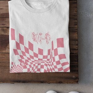 May include: White t-shirt featuring a pink checkered pattern and three cherubs in the centre.