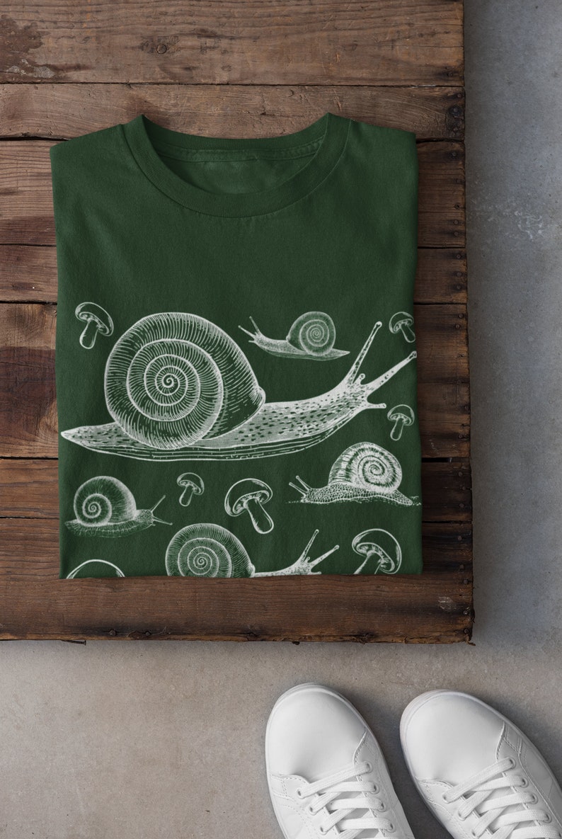 May include: A dark green t-shirt with a white print of snails and mushrooms. The snails are drawn in a vintage style.